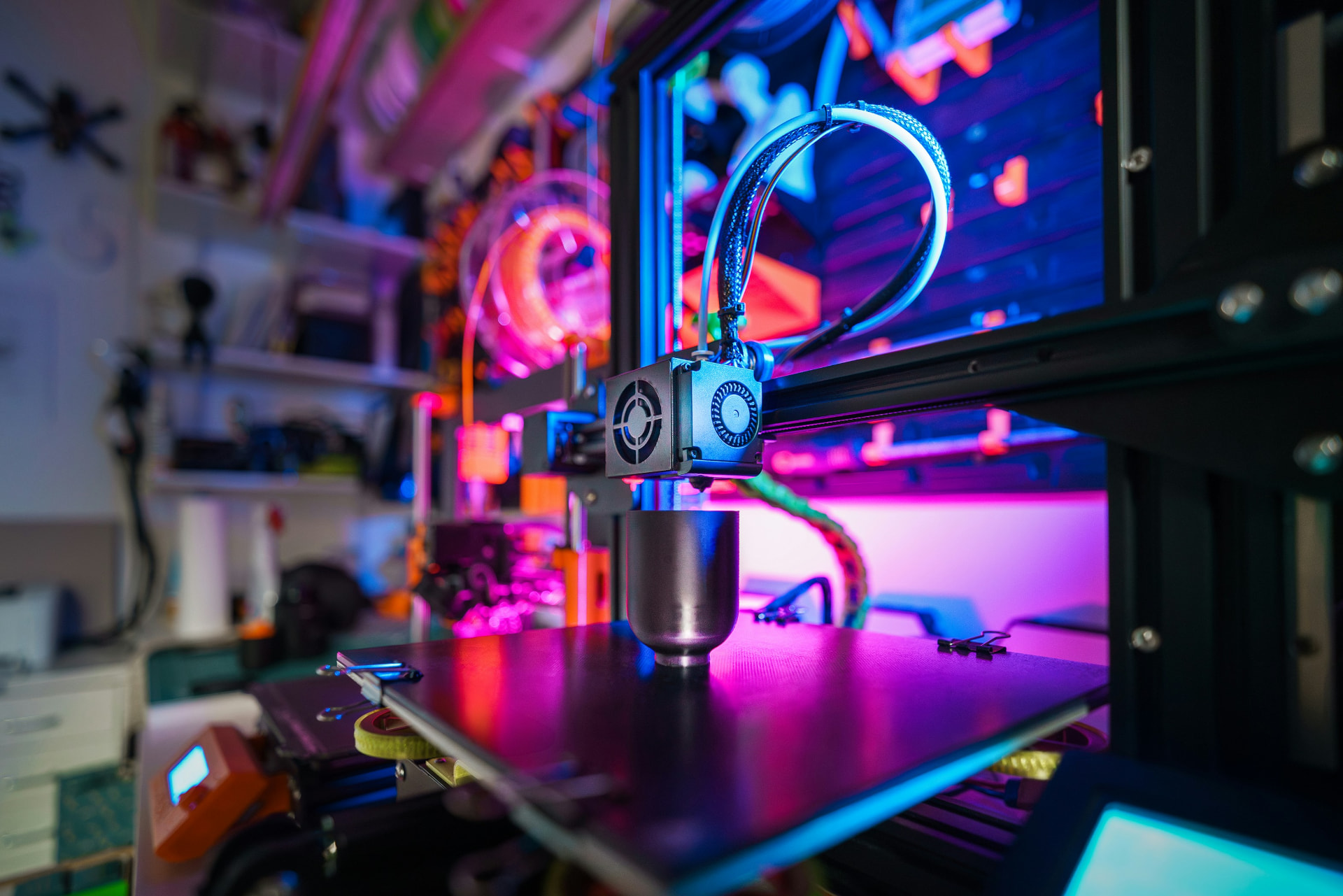 A 3D printer head laying down a printed form under pink and blue light