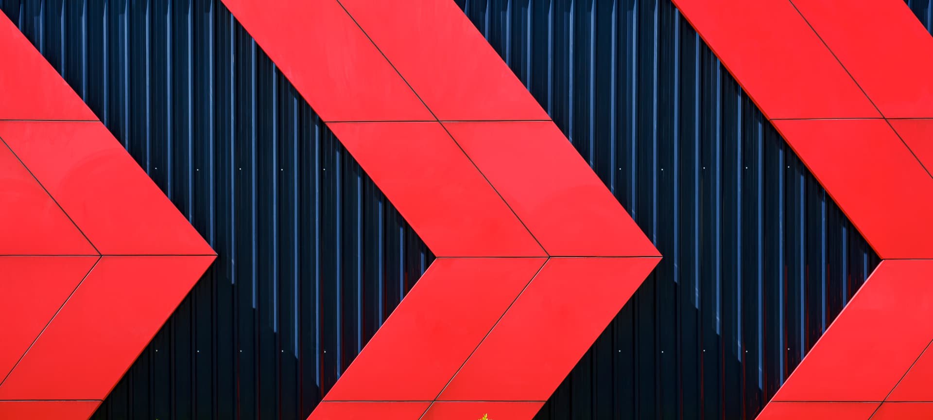 Red chevron arrows pointing forward across a dark ribbed facade