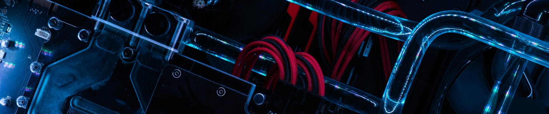 Red braided power cables loop through a dark, blue-lit water-cooled computer build