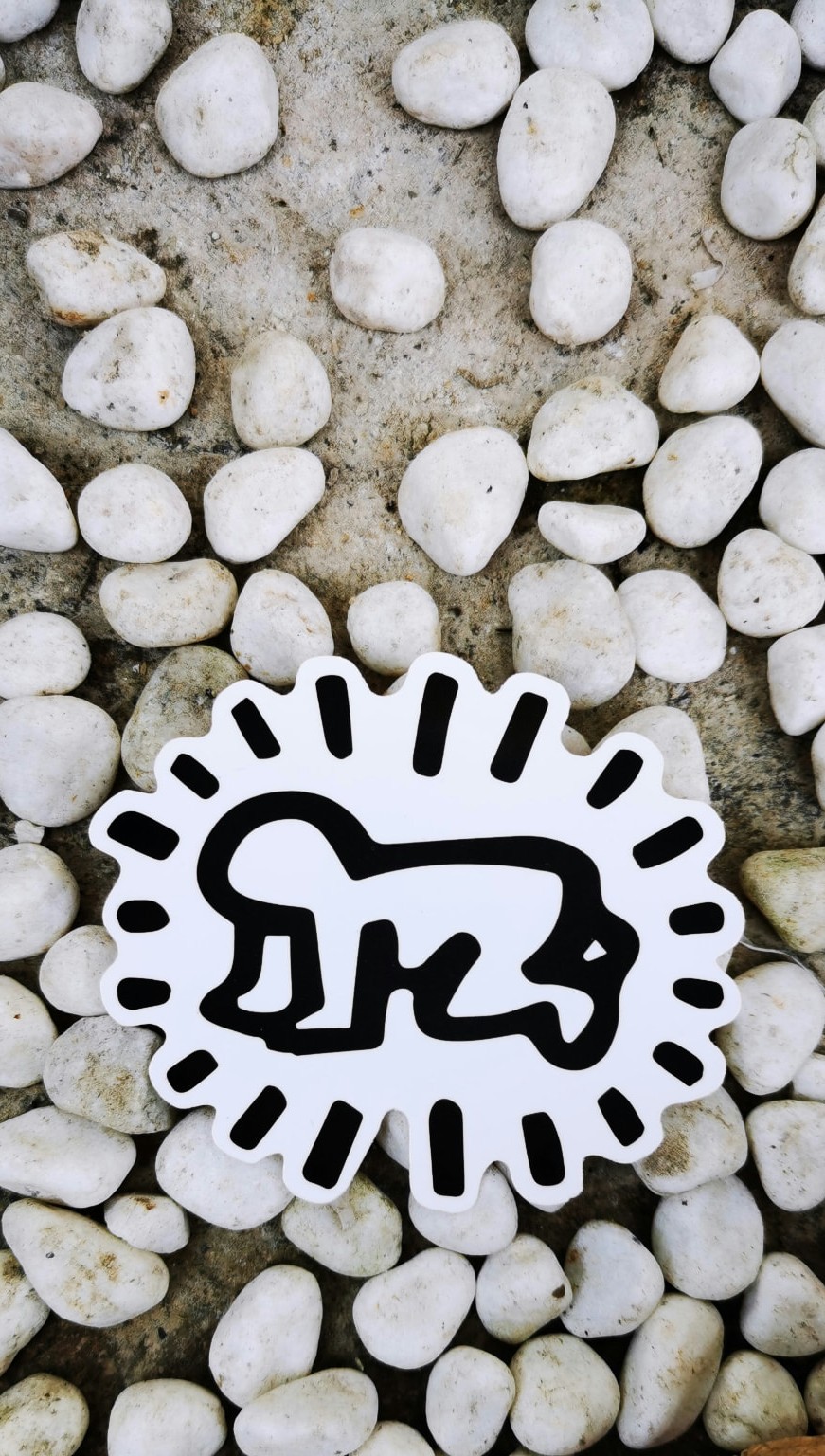 A white die-cut sticker of a crawling baby surrounded by radiating lines, resting on grey pebbles