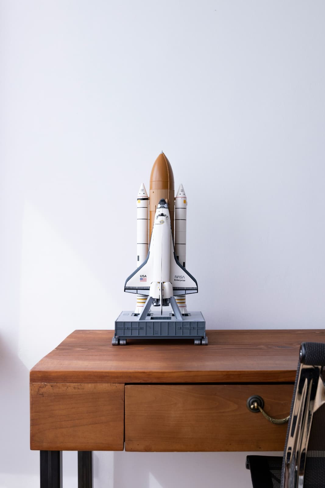 A detailed space shuttle model on a warm wooden desk against a clean white backdrop