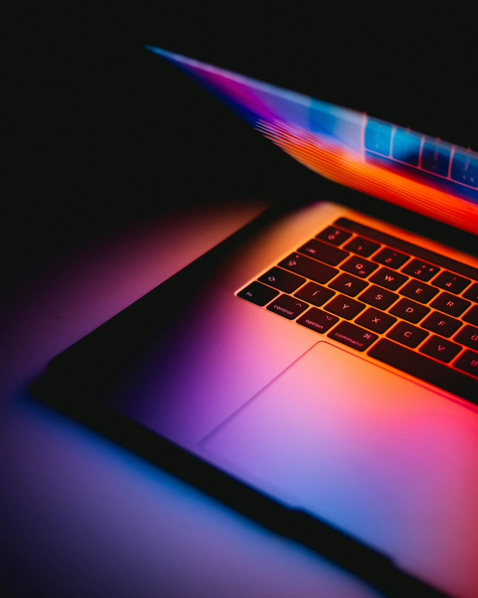 A laptop close-up lit by neon orange, purple and blue light