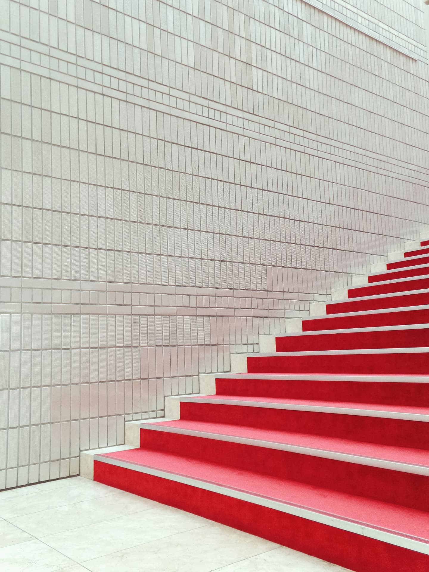 A red-carpeted staircase rising beside a pale tiled wall